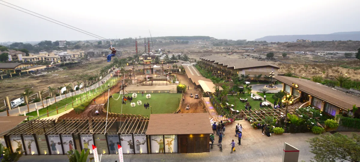 Aerial view of Della Adventure at dusk: a rider on the flying fox above the ATV track, zorbing lawn and activity zones, Lonavala